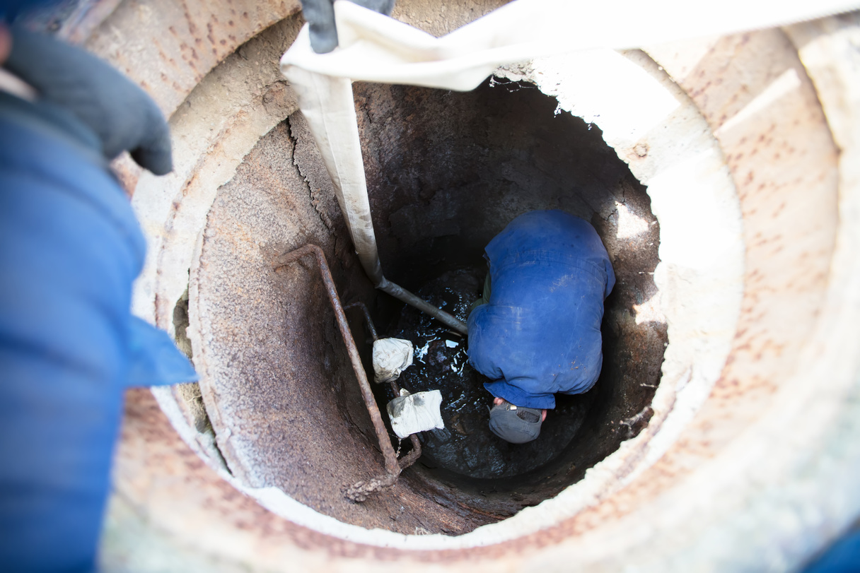 Worker cleans the sewer hatch.A worker cleans a sewer hatch. A man in the hatch.